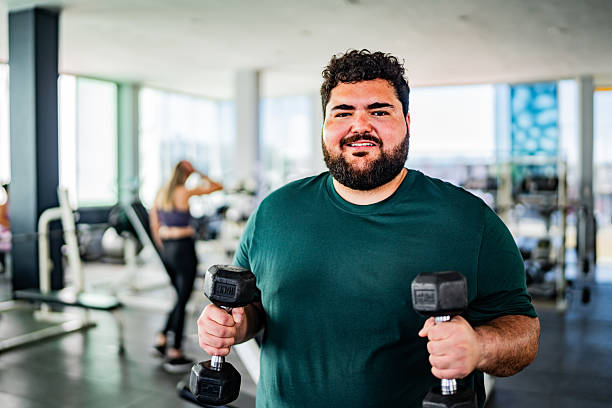 Portrait of mid adult man doing biceps exercises using dumbbell at gym